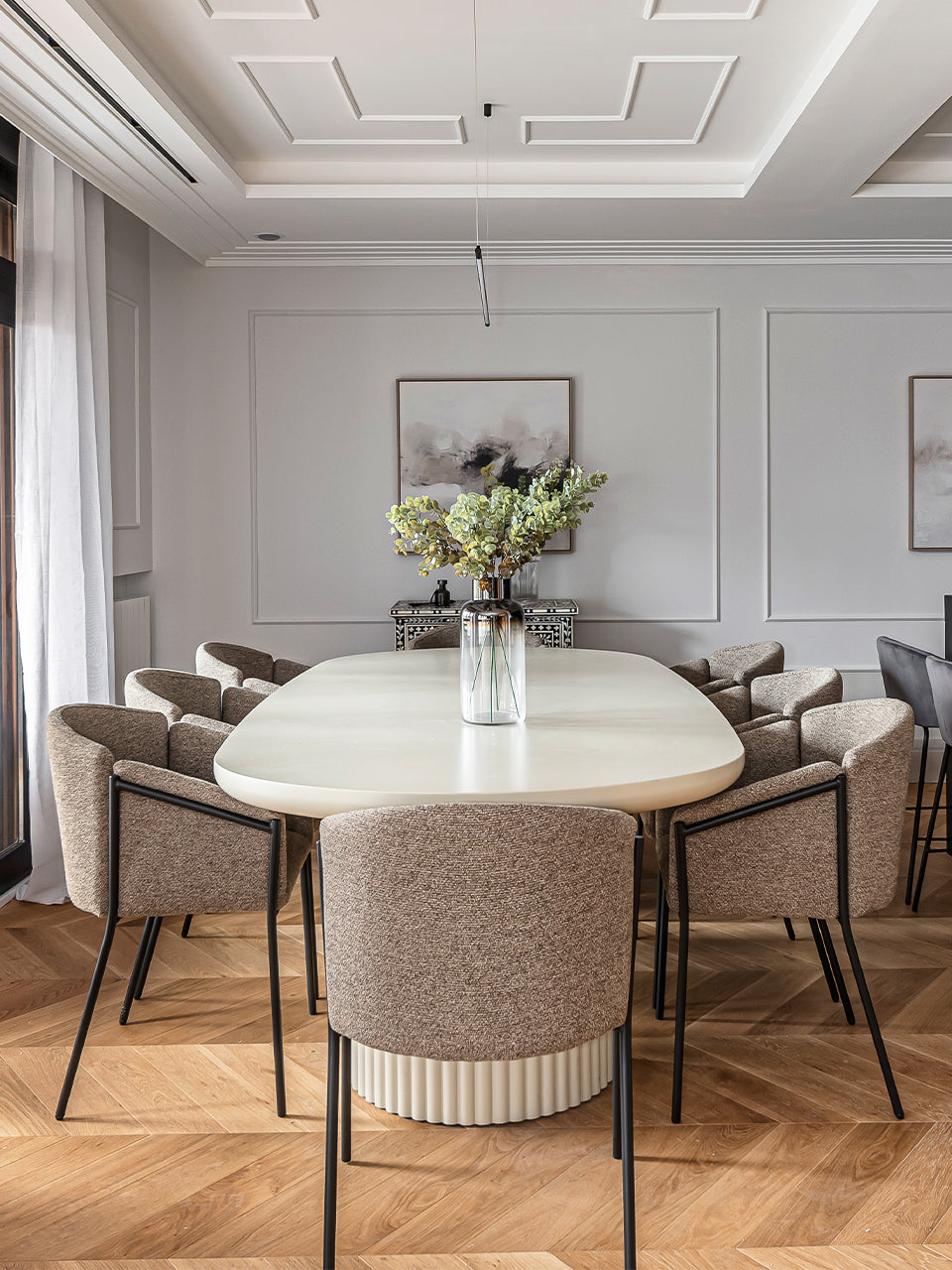 Mesa de comedor ovalada con tablero liso y base acanalada en comedor luminoso.