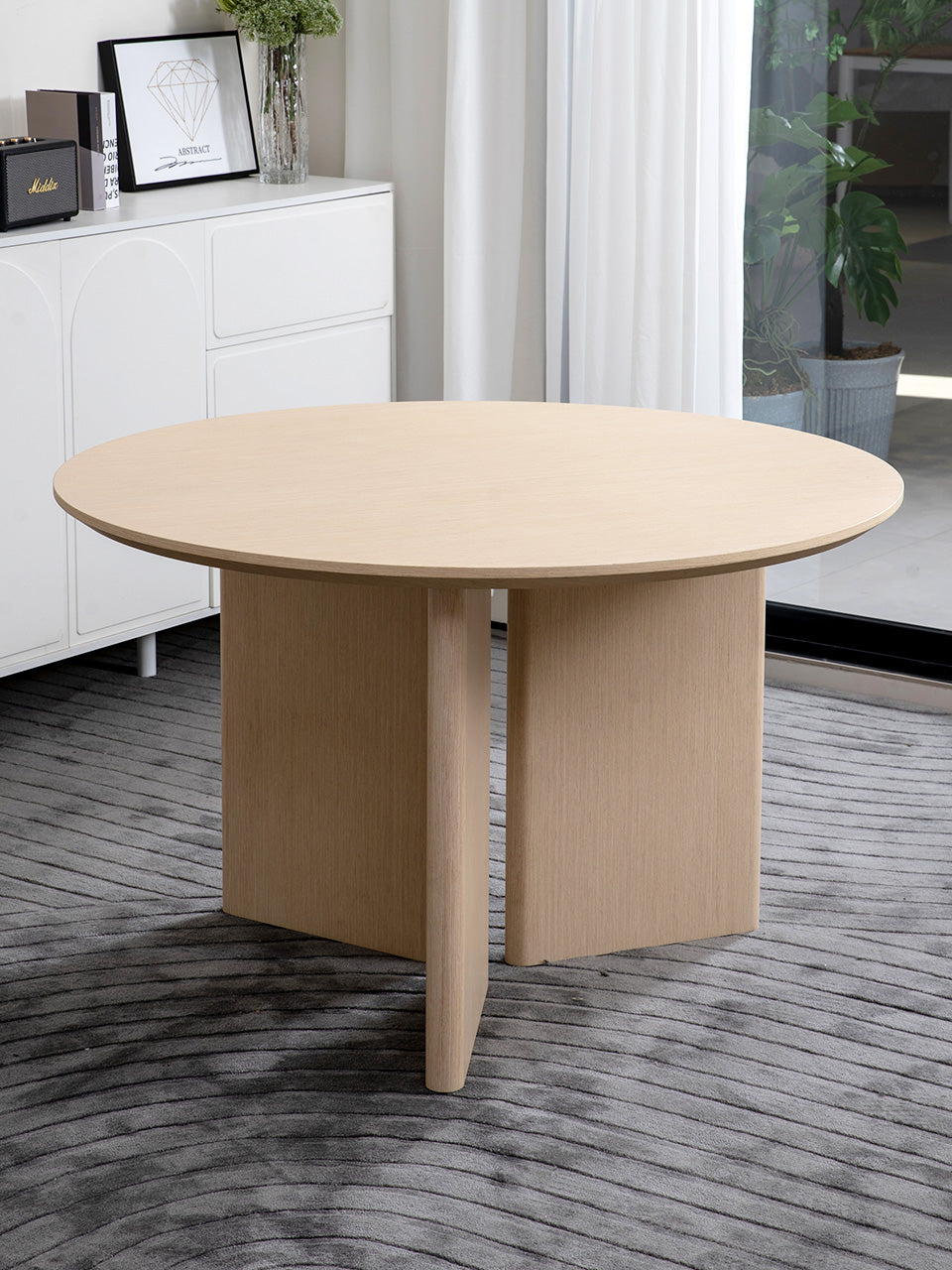 Mesa de comedor en roble natural redonda con tres patas de diseño en salón luminoso.