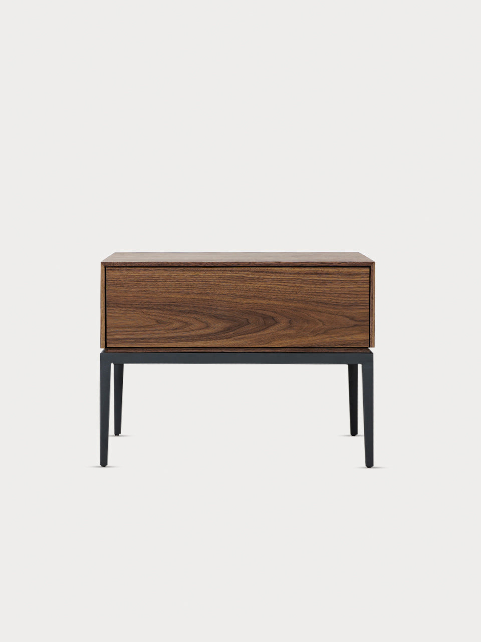 Mesita de noche en madera de nogal con un cajón y soporte metálico en negro mate en vista frontal.