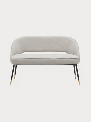 Banco de tejido beige con patas metalizadas en negro y dorado en vista frontal