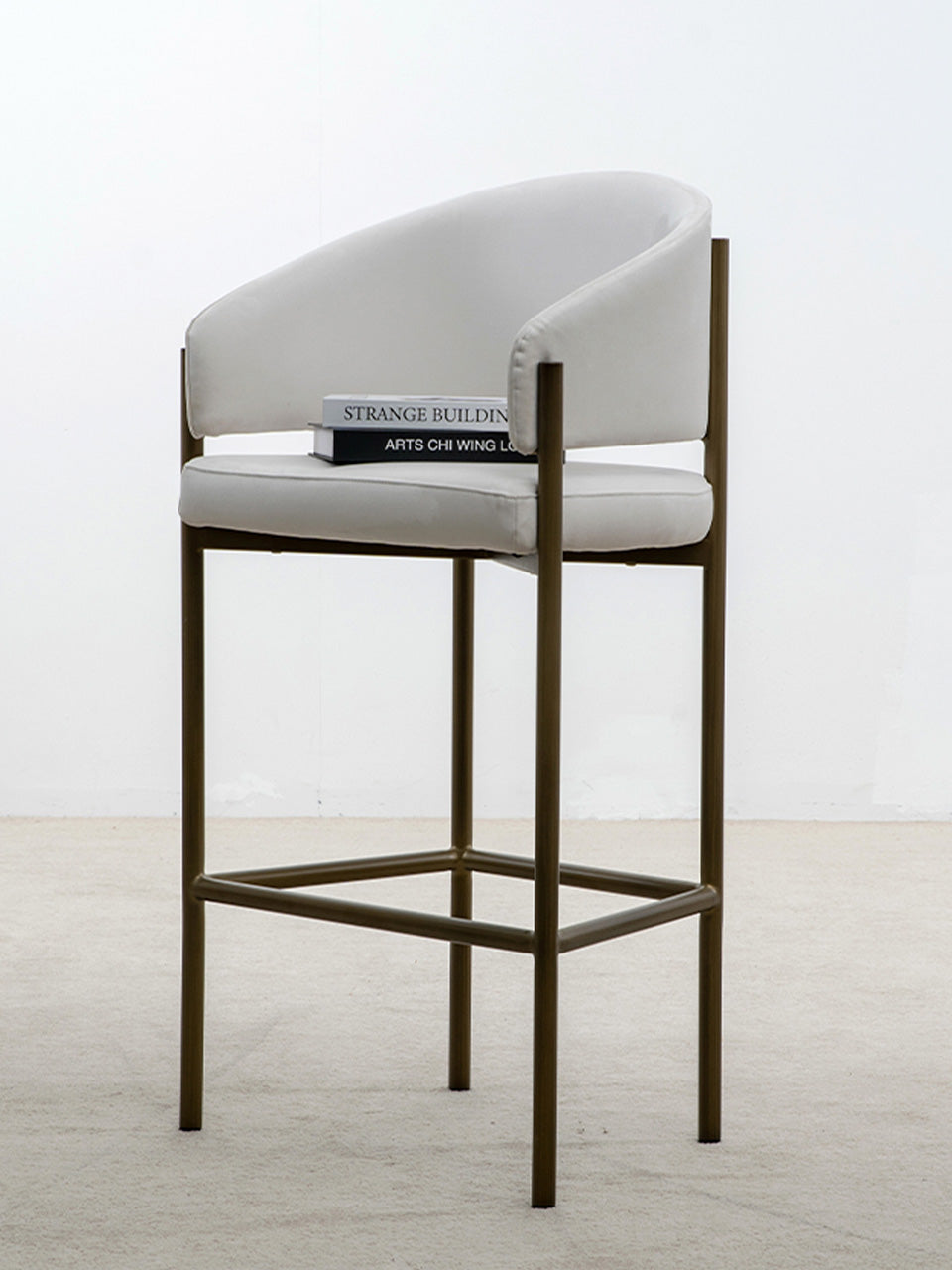 Taburete alto en tejido de tela de ante beige y patas metalizadas con dos libros sobre asiento.