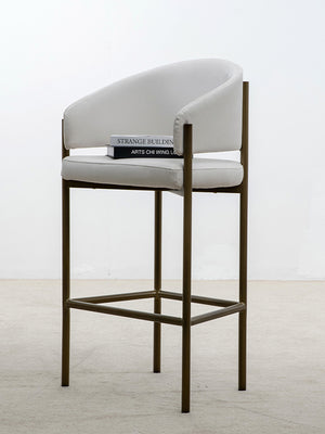 Taburete alto en tejido de tela de ante beige y patas metalizadas con dos libros sobre asiento.